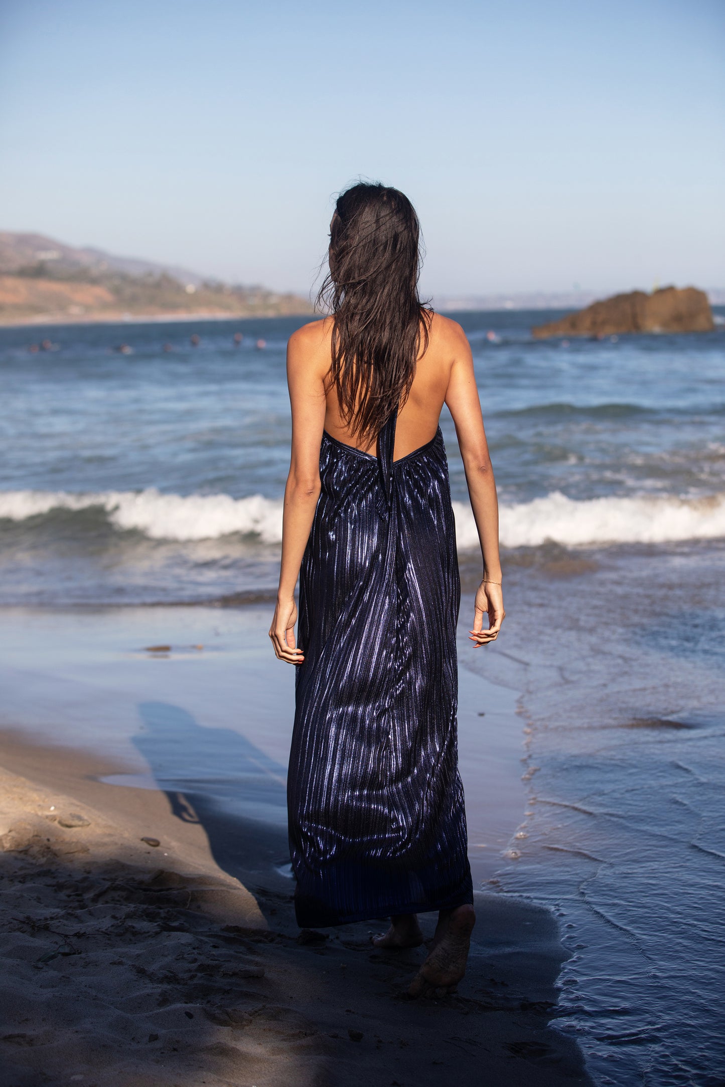 Be the belle of the ball in this Metallic Pleat Halter Gown. A timeless blend of retro vintage chic and glamorous allure, it's crafted from a pleated Lamé metallic fabric with a flowy light weight hand feel. The halter tie features elegant hardware, and the low V back adds a flirtatious touch. A perfect combination for a Resort Getaway or Guest of style to feel your best in. Specialty colors available.