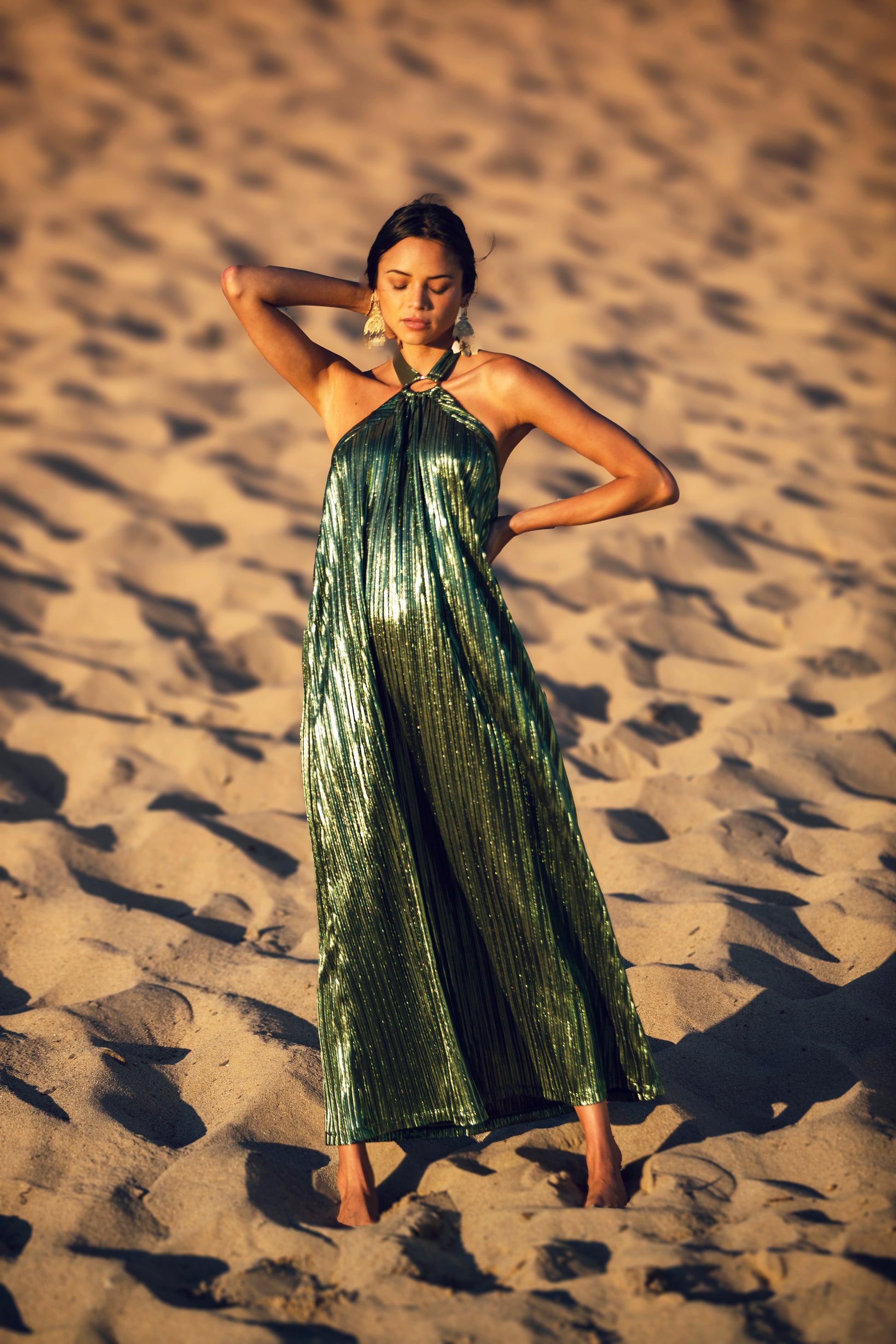 Be the belle of the ball in this Metallic Pleat Halter Gown. A timeless blend of retro vintage chic and glamorous allure, it's crafted from a pleated Lamé metallic fabric with a flowy light weight hand feel. The halter tie features elegant hardware, and the low V back adds a flirtatious touch. A perfect combination for a Resort Getaway or Guest of style to feel your best in. Specialty colors available. 