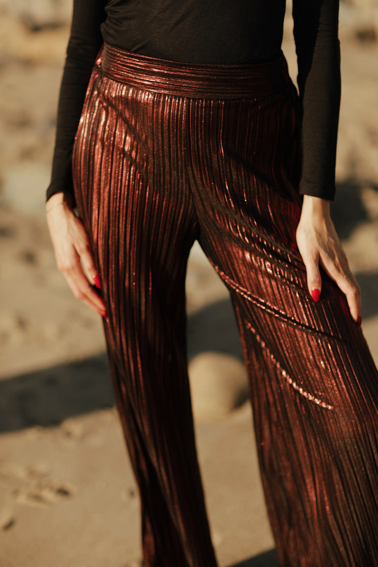These metallic pleated wide leg pants will make any occasion sparkle. Crafted with an elastic back waistband for comfort, this loose-fit design has a high rise with a clean front waistband and flattering pleats throughout. An exclusive and elegant addition to your wardrobe. Complete the look and pair back to our Wrap Collar Top for a classic Fall look. 